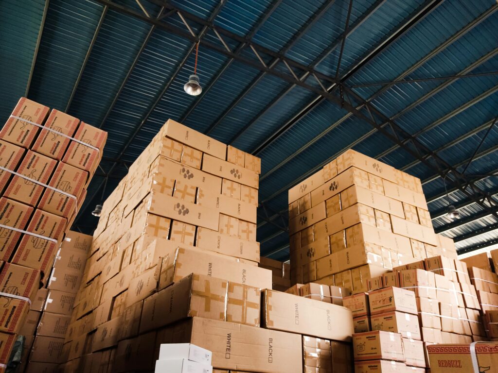 pexels-photo-10834810-10834810 High stacks of cardboard boxes organized in a warehouse with a blue metal ceiling.